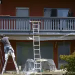 Professional painter preparing exterior surface for a flawless paint job using ladder and protective foil.