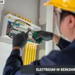 A man wearing a hard hat and gloves is engaged in electrical work on a panel, showcasing his skills in Berkshire.
