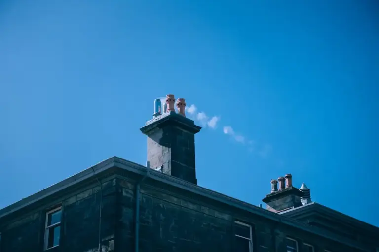 Expert Tips for Maintaining a Healthy Chimney System A plume of smoke rises from a chimney system on the roof of a stone building under a clear blue sky.