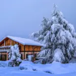 A house in deep snow in winter, with snow on the roof and trees