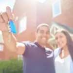 A first-time buyer couple holding house keys outside their new home