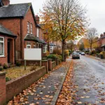 Red-brick terraced houses on a British street in autumn with fallen leaves and a blank estate agent board