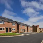 New-build homes with solar panels on a UK housing development under a blue sky